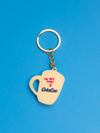 Llavero de The90sisters x ColaCao, hecho en metacrilato, representa una taza de colacao en amarillo y con la frase amor a primer grumito. Producto oficial