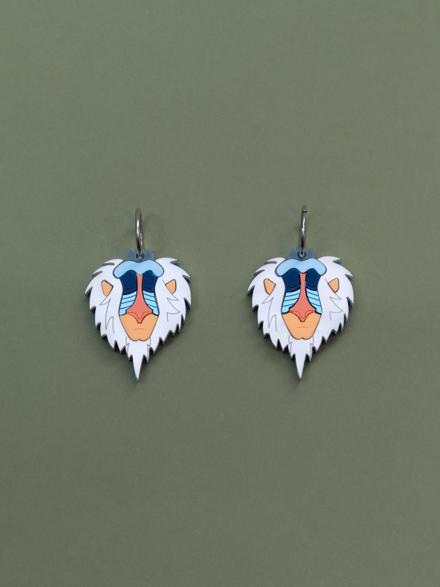 Pendientes inspirados en Rafiki el mandril más querido, en metacrilato blanco aguas naranjas y azules metalicos y brillantes.