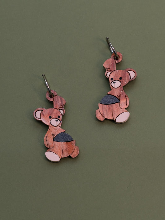 Pendientes de metacrilato inspirados en el osito de peluche de Michael de peter pan, con una bala de cañon en la barriga, en color marrón aguas con purpurina y la bala en negro piedra