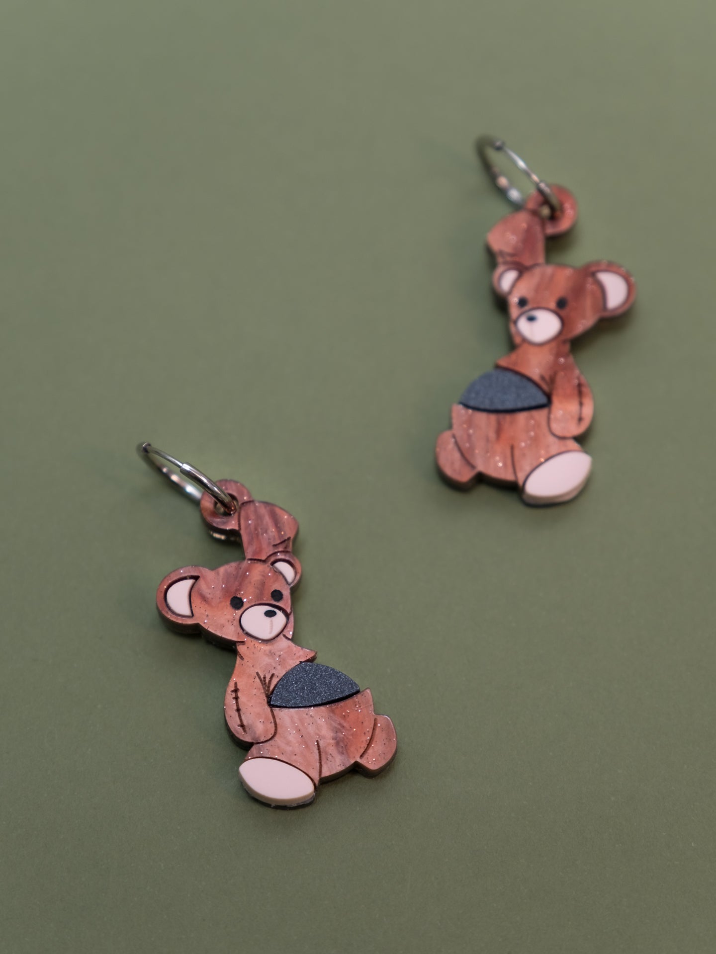Pendientes de metacrilato inspirados en el osito de peluche de Michael de peter pan, con una bala de cañon en la barriga, en color marrón aguas con purpurina y la bala en negro piedra