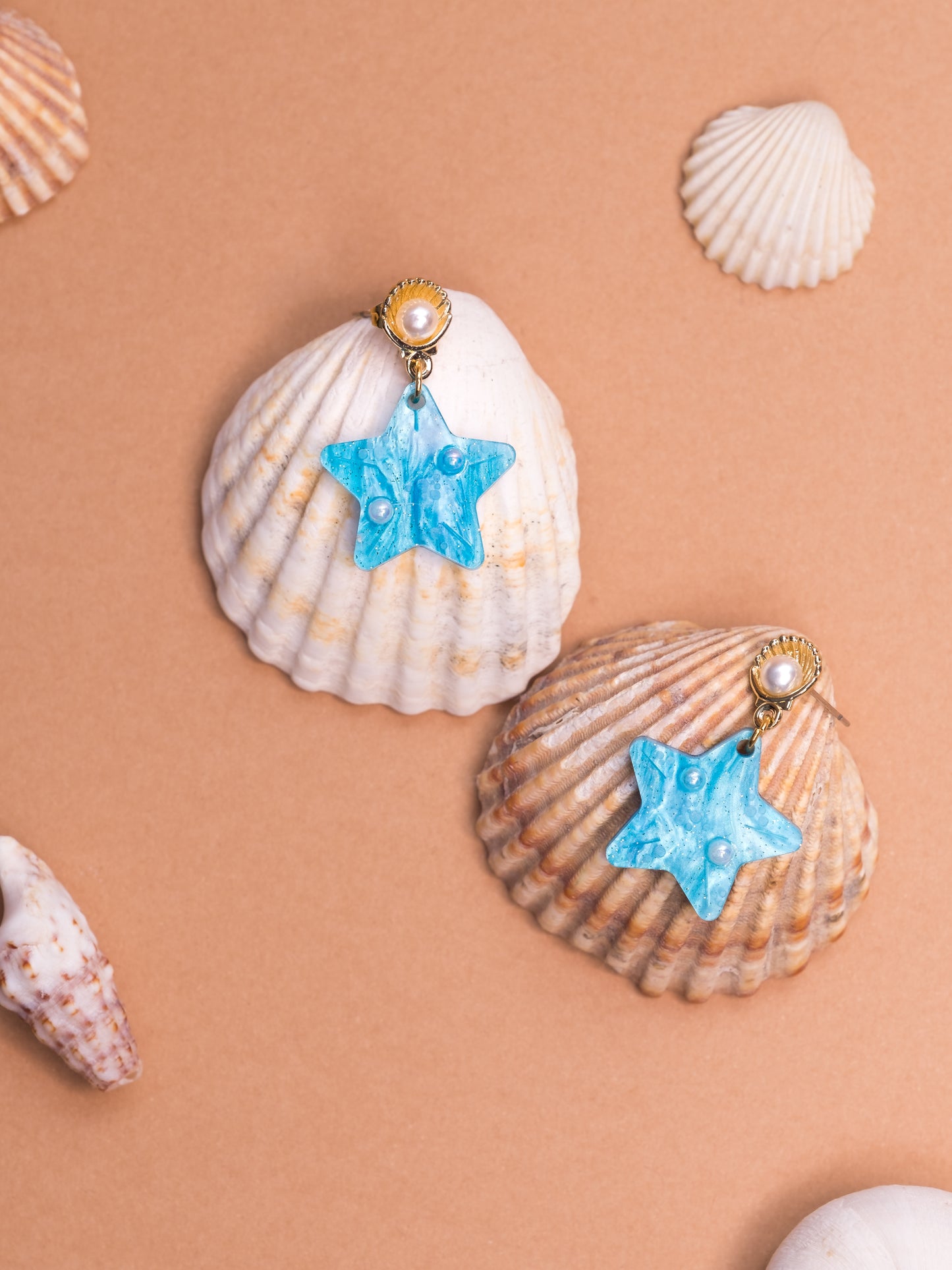 Pendientes de metacrilato azul claro marmolado en forma de estrellita y con detalles de perlas en blanco y dorado ideales para los paseos de las vacaciones en la playa