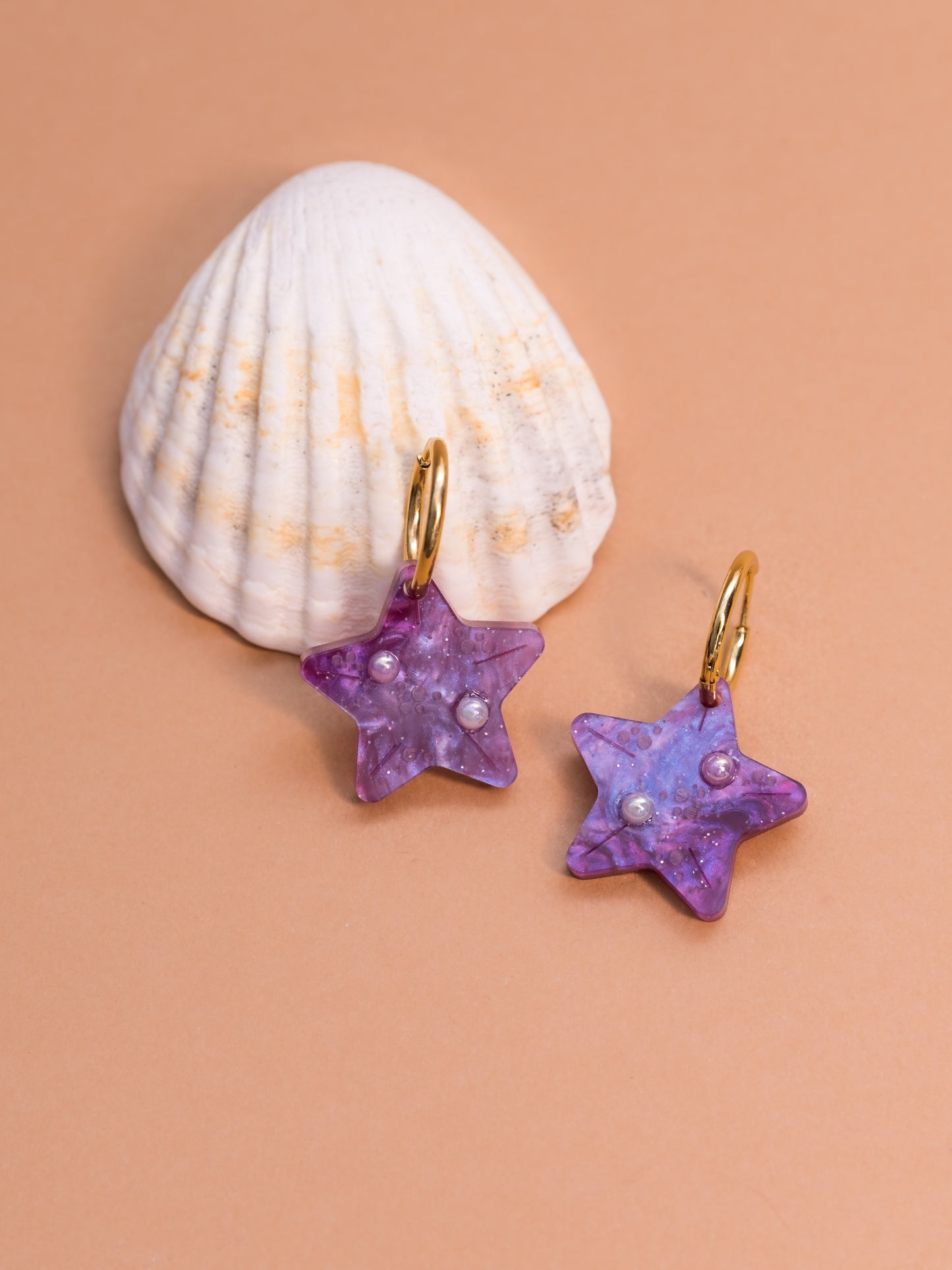 Pendientes de metacrilato morado claro marmolado en forma de estrellita y con detalles de perlas en blanco y dorado ideales para los paseos de las vacaciones en la playa