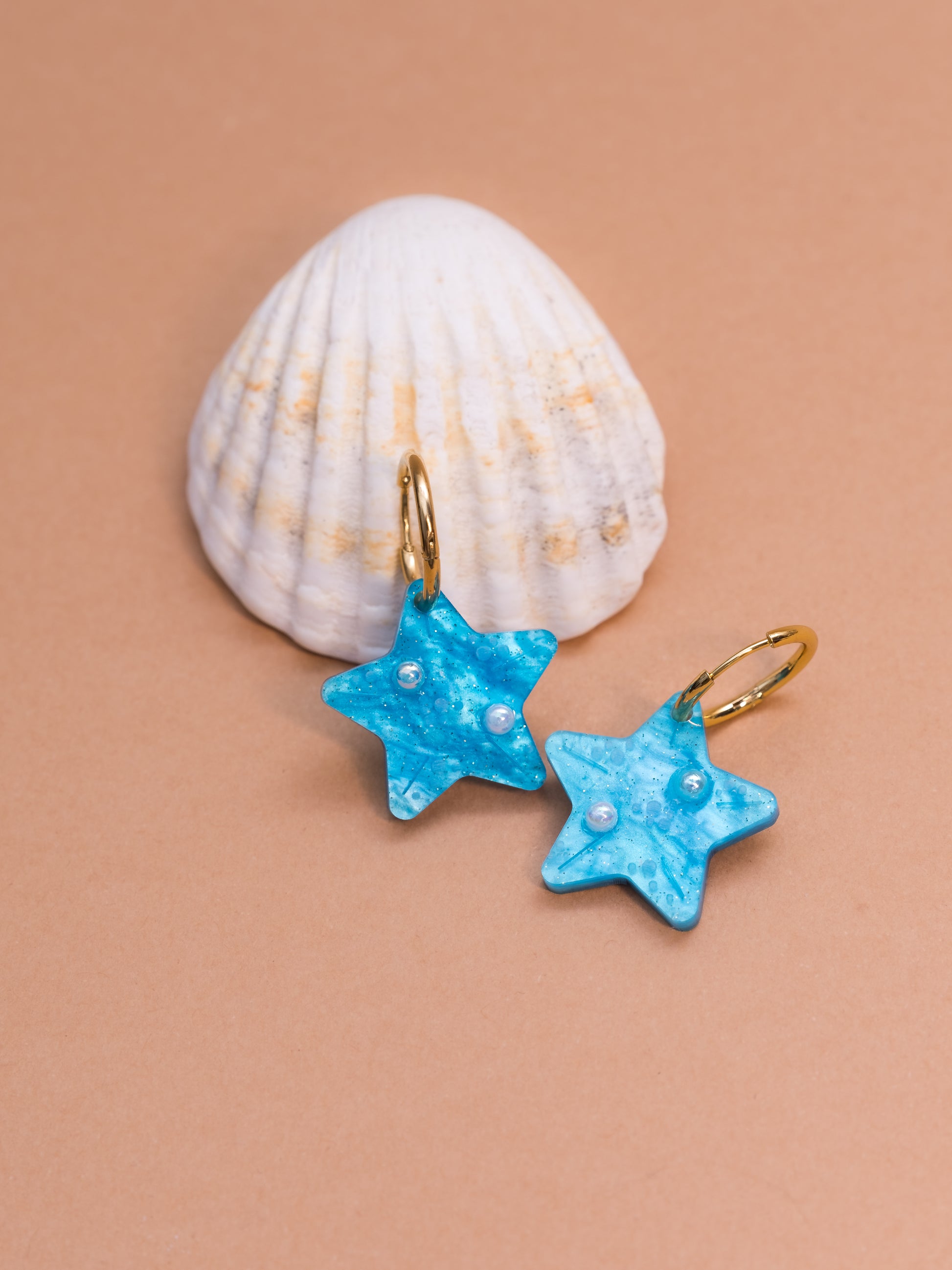 Pendientes de metacrilato azul claro marmolado en forma de estrellita y con detalles de perlas en blanco y dorado ideales para los paseos de las vacaciones en la playa